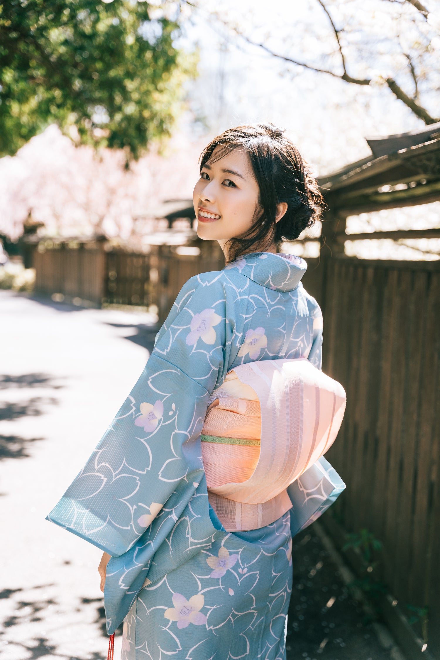 GENEVIEVE CEN in a light blue kimono with floral patterns standing outdoors with cherry blossoms in the background.